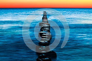 Wooden groynes with blue water and red sunset. Long exposure. photo