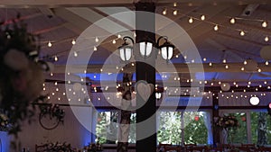 Wooden hall with round lanterns, beams with garlands and multi-colored lighting.