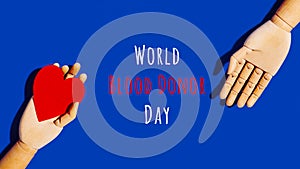 Wooden hand with big red heart in a giving gesture. World Blood Donor Day wording