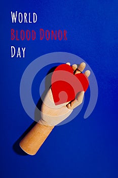 Wooden hand with big red heart in a giving gesture. World Blood Donor Day wording