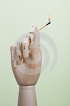 A wooden hand with a lighted match on a colored background