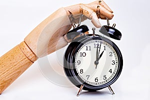 Wooden hand stopping the alarm of a black alarm clock