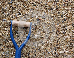 Wooden handle of blue metal garden spade against pebbledash wall