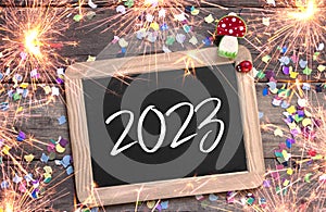 Wooden hang tag and slate with four leaf clover and sparklers with the german words for happy new year - frohes neues jahr 2023 on