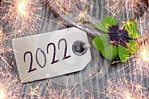 Wooden hang tag and slate with four leaf clover and sparklers with happy new year 2022 on wooden weathered background