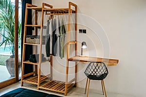 Wooden hangers with clothes on rack and small table with chair in the room