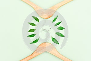 Wooden hangers with green leaves over mint background as a symbol of conscious consumerism, slow fashion