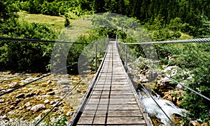 Wooden hanging bridge leading forward over green mountain river.