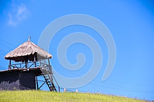 Wooden hay hut roof tower on bright blue sky and green grass hill background