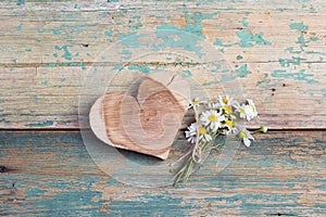 Wooden heart with chamomiles on old turquoise wooden background.