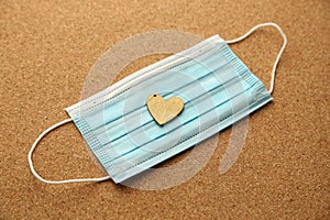 A wooden heart on a medical face mask. Loneliness during the Coronavirus (covid-19) pandemic concept