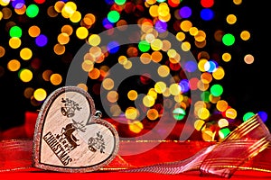 Wooden heart with Merry Christmas text on red ribbon against bokeh background