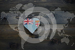 wooden heart with national flag of Fiji near world map on the wooden background