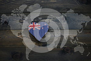 wooden heart with national flag of new zealand near world map on the wooden background