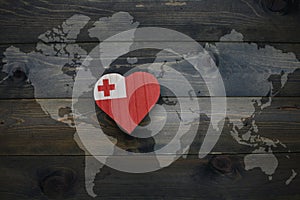 wooden heart with national flag of Tonga near world map on the wooden background