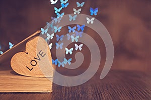 Wooden heart with an old book on the table and a background of bokeh made of butterflies. Valentine`s Day.