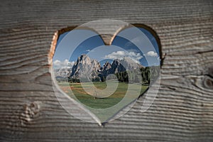 Wooden heart shape with meadows at Alpe di Siusi during summer with view to mountains of Plattkofel and Langkofel in the Dolomite