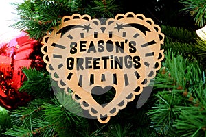 Wooden Heart Shaped Ornament with the Words SEASON`S GREETINGS on Christmas Tree