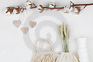 Wooden hearts handing on cotton flower and eco natural paper cups, string bag, wheat on white background