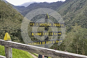 Wooden hiking signposts in Cocora Valley, forested mountains in background, Colombia