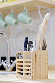 Wooden holder organizer for kitchen tools utensils spoons, knives and spatula on countertop in the modern kitchen