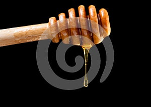 Wooden honey dipper with drop honey black background