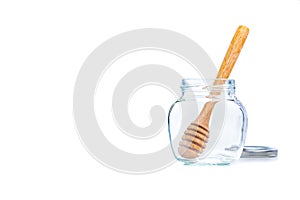 Wooden honey dipper in an empty clear glass jar on white background