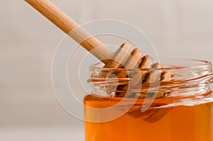A wooden honey spoon and a glass jar with polyfloral golden honey
