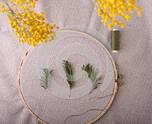 Wooden hoop for needlework with linen fabric, on which green twigs, a needle and a spool of green threads are laid out