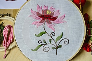 Wooden hoops with an embroidered flower of red and pink petals on branches with leaves on a white fabric on a black background