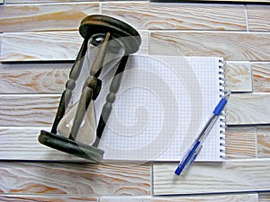 Wooden hourglass, pen and agenda on the wooden background