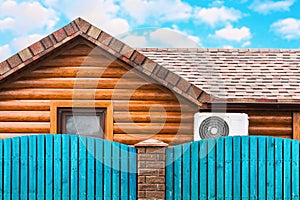 Wooden house with air conditioning, surrounded by a blue fence. Blue sky with clouds