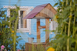 Wooden house with blue facade and white frames on the windows and old wooden well