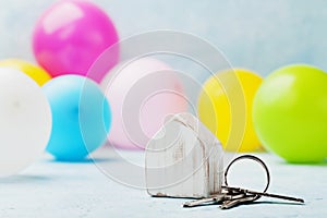 Wooden house with bunch of keys and air balloons on light table. Housewarming, moving, real estate or buying a new home concept.