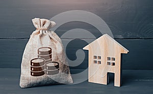 Wooden house and cash coins money bag. Buying and selling real estate. Taxes. Mortgage loan. Sale of housing. Proposal for a deal