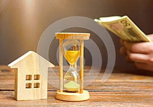 Wooden house and clock. Businessman counting money. Payment of deposit or advance payment for renting a home or apartment. Long-