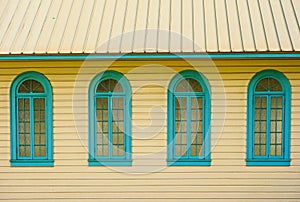 Wooden house facade with yellow walls and blue windows