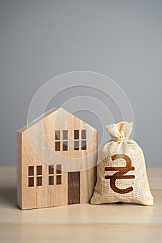 Wooden house figure and ukrainian hryvnia money bag. Taxes. Property value appraisal. Make a deal. Buying and selling real estate