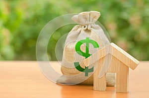 Wooden house figurine and money bag on the background of nature. Mortgage loan for the purchase of housing, construction or