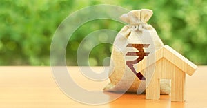 Wooden house figurine and money bag with indian rupee INR symbol. Budget, subsidized funds. Mortgage loan for purchase housing, photo