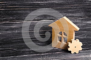 Wooden house with a gear on a background of dark wood. The concept of the enterprise for production, manufactory. Repair