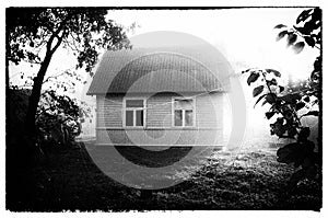 Wooden house and gossamer in foggy morning. Vintage photo imitation.