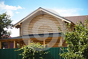 A wooden house with a grey roof behind a green fence with plants growing on it