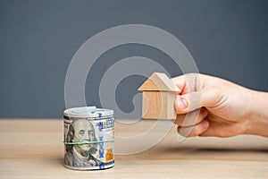 Wooden house in hands and money dollar bills. The concept of attracting investment in real estate. Mortgages and home loans.