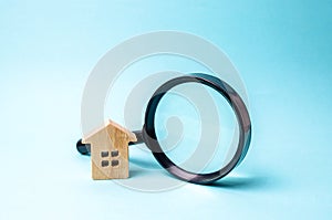 Wooden house and magnifying glass on a blue background. The concept of urban planning, infrastructure projects. Buying and selling