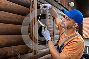 Wooden house maintenance concept. Man holding screwdriver to fix pull handle on wooden shutter