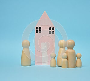 Wooden house and miniature figurines of a family on a blue background. The concept of selling and buying real estate