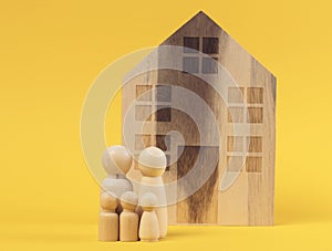 Wooden house and miniature figurines of a family on a yellow background. The concept of selling and buying real estate