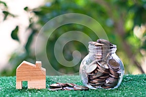 Wooden house model and glass jar with coins inside. Home mortgage and property investment concept. Copy space