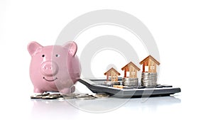 Wooden house model that is on a money stack including pink piggy bank on white background.